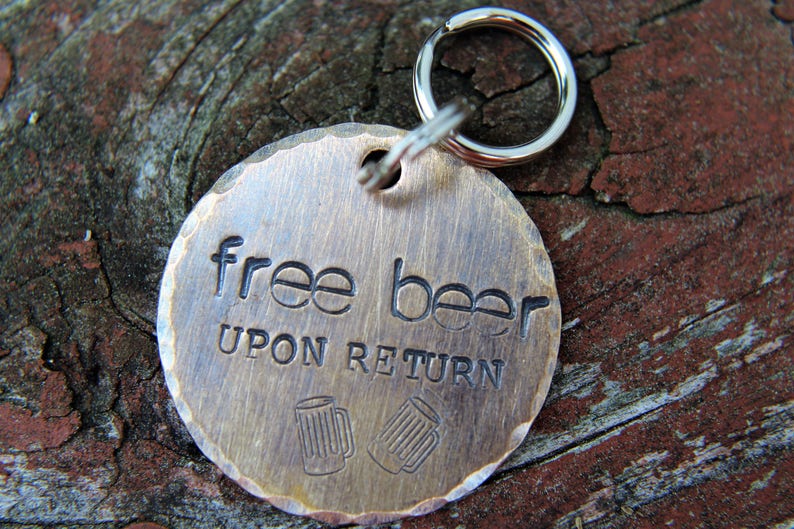 May include: A round, brass-colored tag with the words "free beer upon return" engraved on it. The tag is attached to a silver key ring.