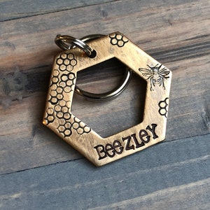 May include: A gold hexagonal key chain with a bee design and the name "Beezley" engraved on it.