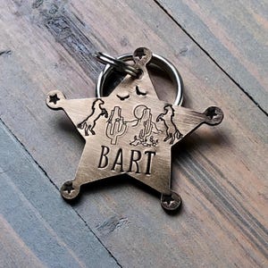 May include: A bronze star-shaped keychain with a cowboy theme. The keychain features two horses, cacti, and the name "BART" engraved on the front.