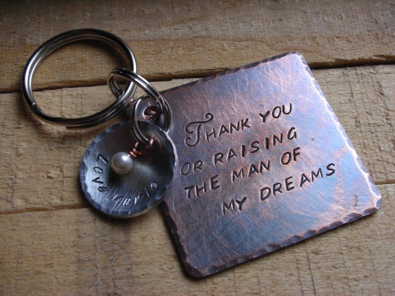 May include: A copper-toned metal keychain with a square tag that reads "Thank you for raising the man of my dreams". The keychain also has a round charm with the word "Love" engraved on it.