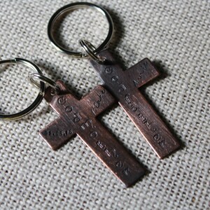 Pu&ograve; includere: Due portachiavi a forma di croce in rame con testo inciso. Il testo sul portachiavi sinistro recita "Go forth and make a difference" e il testo sul portachiavi destro recita "God is always with you".
