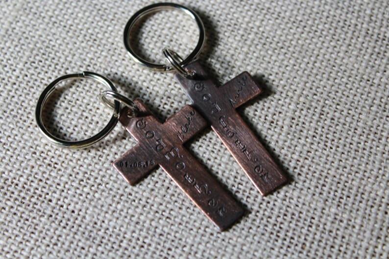 Pu&ograve; includere: Due portachiavi a forma di croce in rame con testo inciso. Il testo sul portachiavi sinistro recita "Go forth and make a difference" e il testo sul portachiavi destro recita "God is always with you".