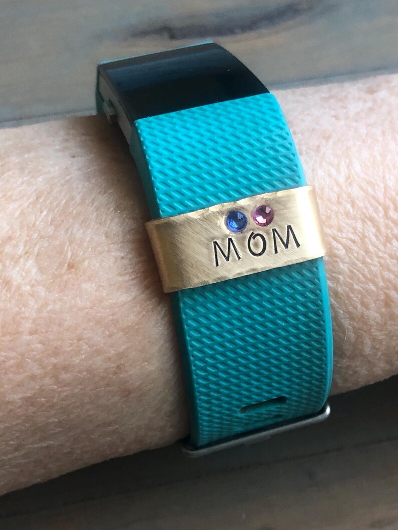 May include: A turquoise fitness tracker with a gold band that says "MOM" with three small gemstones.