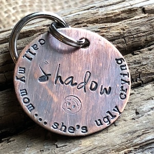 May include: A copper dog tag with a key ring. The tag has the text "Shadow... she's ugly crying... mom,  I'm tired" engraved on it.
