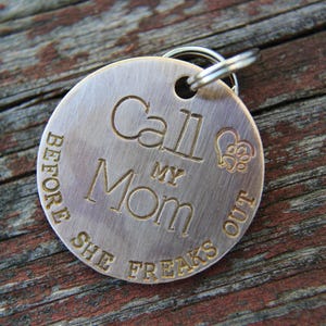 May include: A round, brushed metal pet tag with the engraved text "Call My Mom Before She Freaks Out." The tag includes a paw print and heart design. A silver ring is attached for easy attachment to a pet's collar.