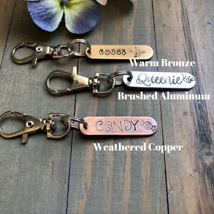 May include: Three keychains with different metal finishes: warm bronze, brushed aluminum, and weathered copper. The keychains feature personalized engravings: "GOOSE", "Queenie", and "CANDY".