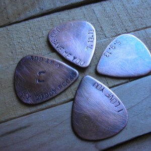 May include: Four copper guitar picks with different engraved messages. The messages are "God Save Me You", "7.13.18", "I Love You", and "C.M.X. 604 Buddy Rocks".