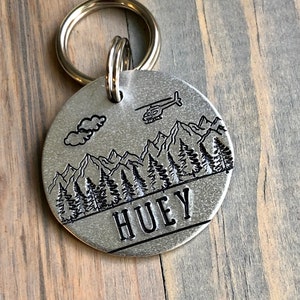 May include: Silver dog tag with a mountain scene and a helicopter. The tag is engraved with the name "HUEY".