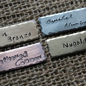 May include: Four metal tags with different finishes and text. The tags read "Warm Bronze", "Brushed Aluminum", "Nugold", and "Weathered Copper".