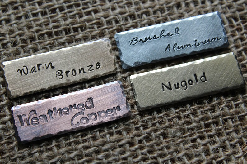 May include: Four metal tags with different finishes and text. The tags read "Warm Bronze", "Brushed Aluminum", "Nugold", and "Weathered Copper".