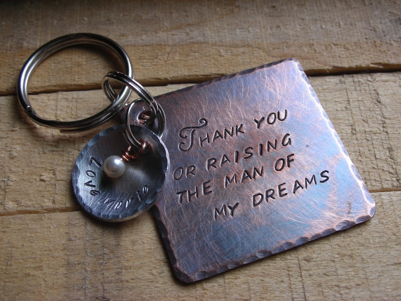 May include: A copper-toned keychain with a square tag that reads "Thank you for raising the man of my dreams". The tag is attached to a silver key ring with a small silver charm that has a pearl and the word "Love" engraved on it.