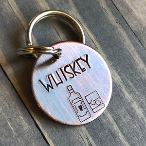 May include: A copper-colored key chain with a round tag that says "WHISKEY" and features a small engraved image of a bottle and a glass of whiskey.