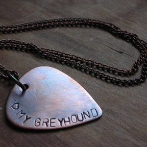 May include: A copper guitar pick necklace with a heart and the words "My Greyhound" engraved on it.