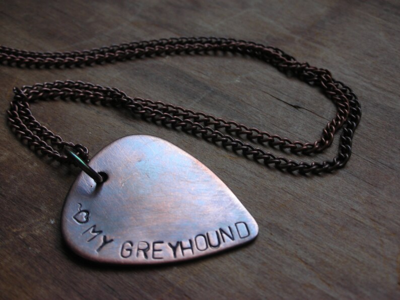 May include: A copper guitar pick necklace with a heart and the words "My Greyhound" engraved on it.