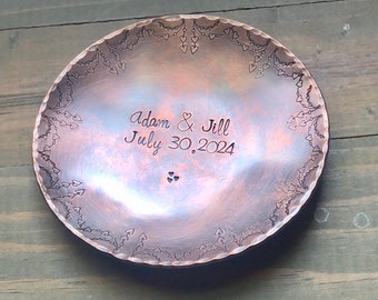May include: A copper ring dish with a heart design border. The dish is engraved with the text "Adam & Jill July 30, 2024".