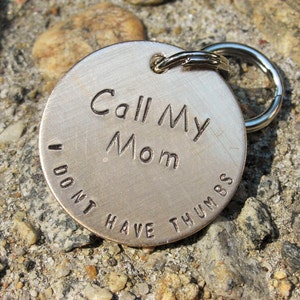May include: Silver dog tag with the text "Call My Mom I Don't Have Thumbs" engraved on it.