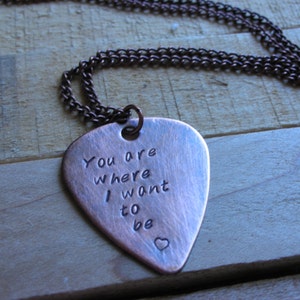 May include: A copper guitar pick necklace with the inscription "You are where I want to be" and a small heart.