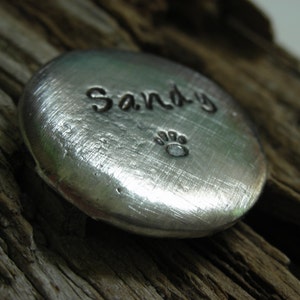 May include: A silver metal charm with the name "Sandy" engraved on it and a paw print below the name.