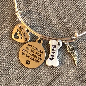 Op de afbeelding: Zilveren armband met bedels die "Beste vriend", "Niet langer aan mijn zijde, maar voor altijd in mijn hart", "Bitzy" en een vleugelbedel zeggen.