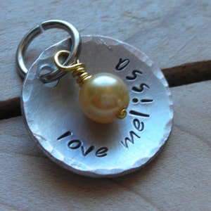 May include: A silver metal dog tag with a hammered finish and a small gold bead. The tag is engraved with the words "love meliss" and has a silver ring for attaching to a collar.