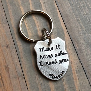 Puede incluir: Llavero de plata con un dije en forma de escudo que dice "Make it home safe. I need you." y un coraz&oacute;n con "Dada" inscrito debajo.