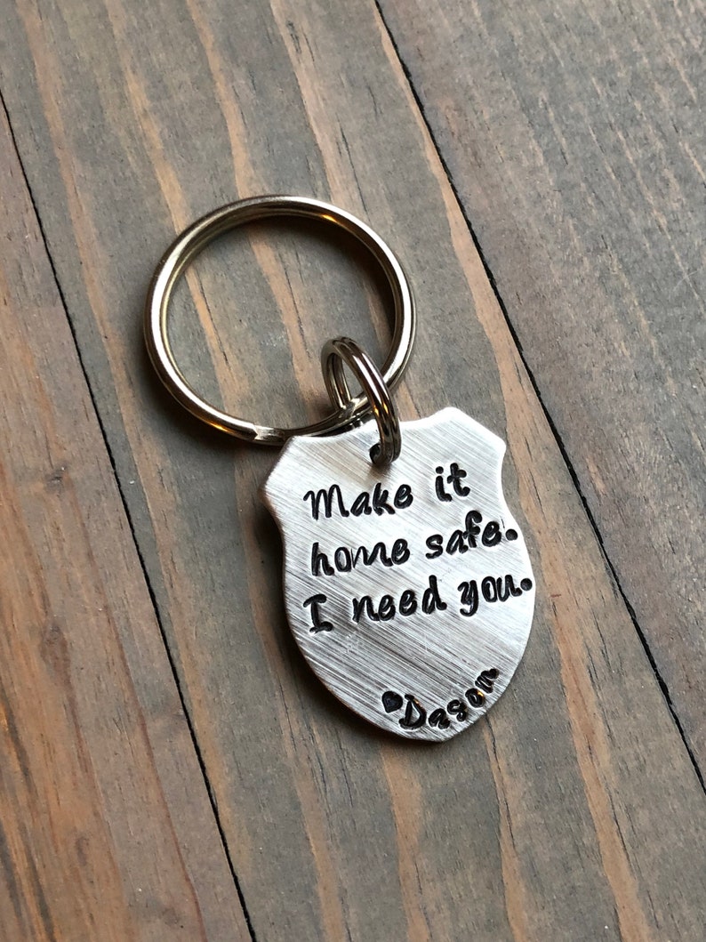 Puede incluir: Llavero de plata con un dije en forma de escudo que dice "Make it home safe. I need you." y un coraz&oacute;n con "Dada" inscrito debajo.