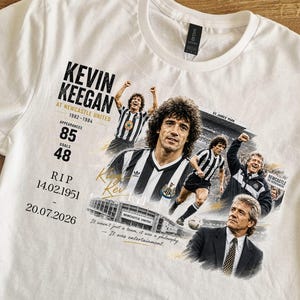 Może przedstawiać: Biały t-shirt z nadrukiem graficznym przedstawiającym Kevina Keegana w Newcastle United. Projekt zawiera kilka zdjęć zawodnika, tekst "Kevin Keegan at Newcastle United 1982-1984", "Appearances 85", "Goals 48", "RIP 14.02.1951 - 20.07.2026" oraz "It wasn't just a team, it was a philosophy - It was entertainment."