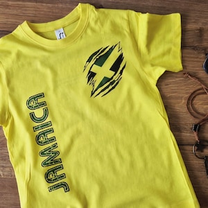 May include: Yellow t-shirt with the word "JAMAICA" printed vertically in green. The shirt features a torn design with a cross in the center. Sunglasses and a necklace with a feather pendant are also visible.