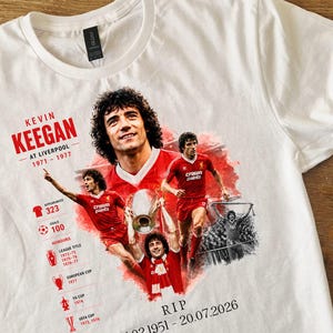 Może przedstawiać: Biały t-shirt z nadrukiem graficznym przedstawiającym Kevina Keegana w stroju Liverpoolu. Projekt zawiera wiele zdjęć zawodnika, tekst KEVIN KEEGAN AT LIVERPOOL 1971-1977, statystyki kariery, ikony trofeów oraz napis RIP 1951-20.07.2026.