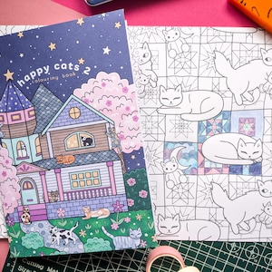 K&ouml;nnte beinhalten: Ein Malbuch "Happy Cats 2" mit einer Hausillustration und einer Seite mit Katzenzeichnungen. Das Cover zeigt ein Haus mit Katzen, Sternen und dem Text "Happy Cats 2 colouring book". Die offene Seite zeigt Katzenumrisse.