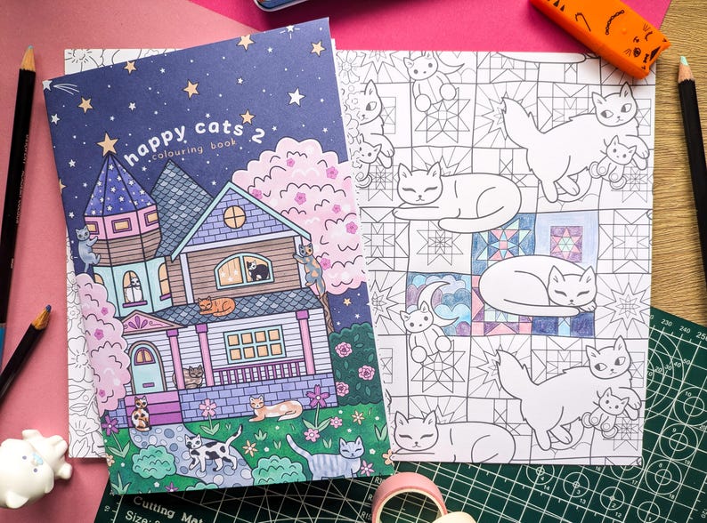 K&ouml;nnte beinhalten: Ein Malbuch "Happy Cats 2" mit einer Hausillustration und einer Seite mit Katzenzeichnungen. Das Cover zeigt ein Haus mit Katzen, Sternen und dem Text "Happy Cats 2 colouring book". Die offene Seite zeigt Katzenumrisse.