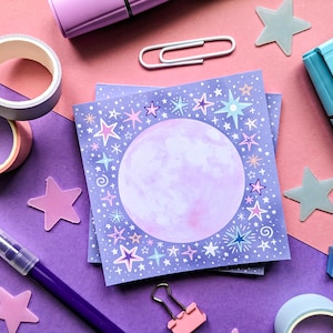 Peut inclure: Un lot de blocs-notes violets et blancs avec un motif de lune et d'étoiles. Les blocs-notes sont sur une surface violette et rose avec d'autres articles de papeterie.