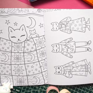 K&ouml;nnte beinhalten: Offene Seiten eines Malbuchs mit Katzenillustrationen. Eine Seite zeigt eine Katze im Bett unter einer Steppdecke mit Sternen und Monden. Die andere Seite zeigt drei Katzen in verschiedenen Outfits. Die Illustrationen sind in Schwarzwei&szlig;.
