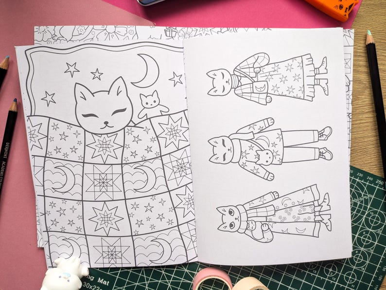 K&ouml;nnte beinhalten: Offene Seiten eines Malbuchs mit Katzenillustrationen. Eine Seite zeigt eine Katze im Bett unter einer Steppdecke mit Sternen und Monden. Die andere Seite zeigt drei Katzen in verschiedenen Outfits. Die Illustrationen sind in Schwarzwei&szlig;.