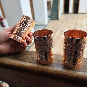 Lifestyle shot of the copper cups on a wooden table, featuring all three designs.