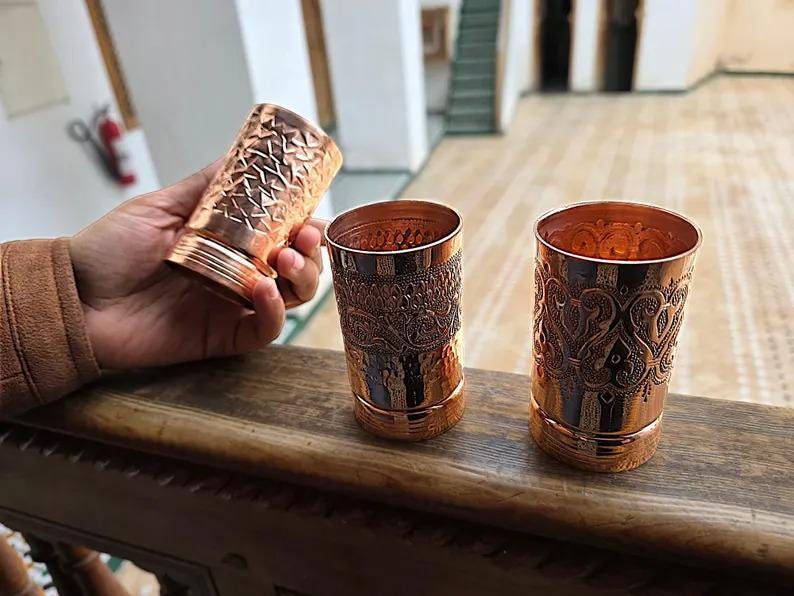 Lifestyle shot of the copper cups on a wooden table, featuring all three designs.