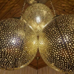 Three globe Moroccan brass chandelier hanging from a wooden ceiling.