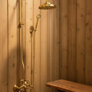May include: A gold-coloured shower fixture with a round showerhead and a handheld showerhead. Water streams from the showerhead. The fixture is mounted on a wooden wall. A wooden bench is in the foreground.