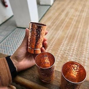 Group of three embossed copper glasses against a soft-focus background.