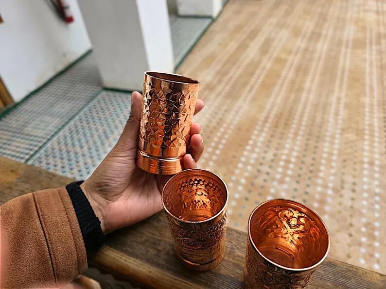 Group of three embossed copper glasses against a soft-focus background.