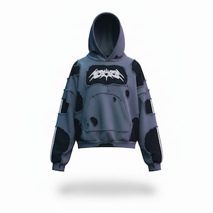 Op de afbeelding: Grijze hoodie met distressed details, een voorzak en een capuchon. De hoodie heeft zwarte patches en witte strepen op de mouwen. Een wit logo staat op de borst.