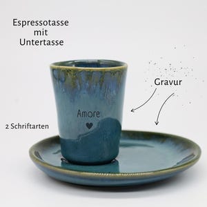 Può includere: Un set di tazzina da espresso e piattino in ceramica blu con finitura smaltata reattiva. La tazzina presenta il testo inciso "Amore" sopra un piccolo simbolo a forma di cuore. Il testo nell'immagine include "Espressotasse mit Untertasse", "Gravur" e "2 Schriftarten".