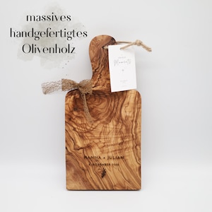 May include: A rectangular olive wood serving board with a handle, featuring a natural wood grain pattern. The board is engraved with the text HANNA + JULIAN and 8 NOVEMBER 2025. It is decorated with a brown mesh ribbon and a white tag labeled Unique Moments.