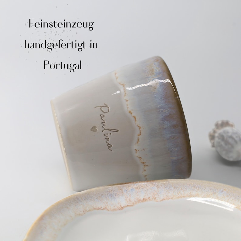 May include: A ceramic mug with a white base and a gradient of blue and brown at the rim. The mug has the name "Paulina" written on it, along with a small heart. The text "Feinsteinzeug handgefertigt in Portugal" is also visible.