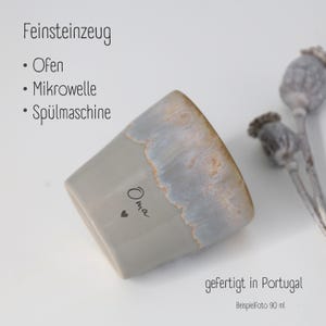 May include: A grey stoneware cup with a reactive glaze rim, featuring the text 'Oma' and a small heart icon. The text 'Feinsteinzeug', 'Ofen', 'Mikrowelle', 'Sp&uuml;lmaschine', 'gefertigt in Portugal', and 'Beispielfoto 90 ml' is visible on the image.