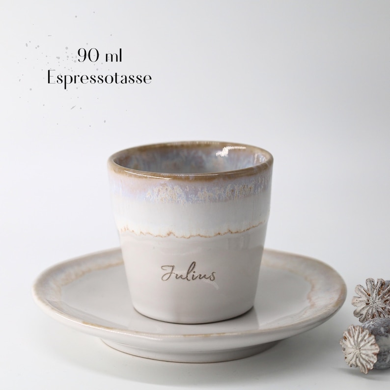 May include: A ceramic espresso cup and saucer set. The cup is white with a light brown rim and a gray base, and the saucer is white. The cup has the name "Julius" printed on it. The text "90 ml Espressotasse" is above the cup.