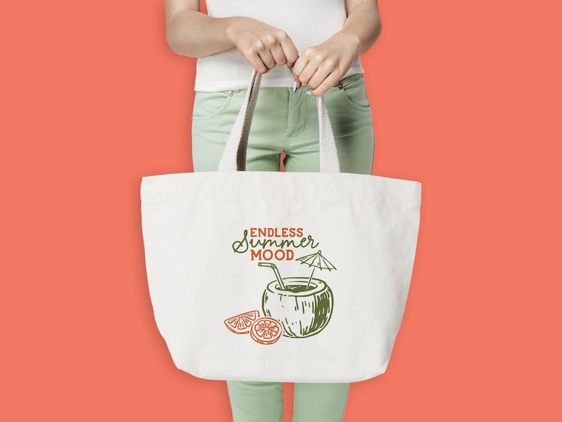 May include: A white tote bag with a cream-colored handle is held by a person. The bag features a green and orange illustration of a coconut drink with the words "Endless Summer Mood". The background is a solid coral color.