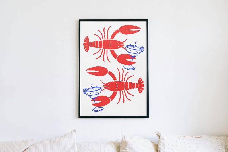 Pu&ograve; includere: Una stampa artistica da parete incorniciata raffigurante due aragoste rosse orientate in direzioni opposte, ognuna delle quali tiene un bicchiere da margarita blu con una fetta di lime. La stampa ha uno sfondo bianco e una cornice nera sottile.