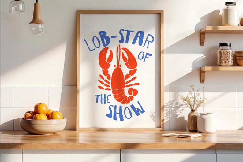 Pu&ograve; includere: Una stampa artistica da parete rettangolare in una cornice di legno chiaro con un'illustrazione di un'aragosta arancione brillante centrata su sfondo bianco con il testo blu LOB-STAR OF THE SHOW arcuato sopra e sotto in stile disegnato.