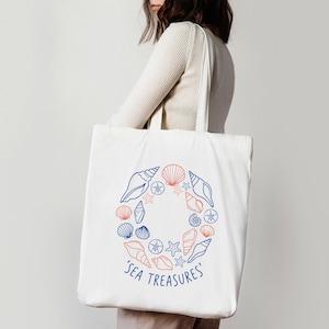 May include: White tote bag featuring a circular design of seashells and starfish in blue and coral. The words 'SEA TREASURES' are printed in blue below the design. The bag has a simple, clean design.